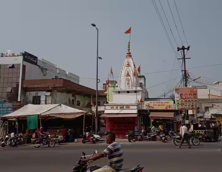 मुख्य सड़क के किनारे स्थित बैरागढ़ काली माता मंदिर और उसके सामने व्यस्त ट्रैफिक और दोपहिया वाहन सवार।