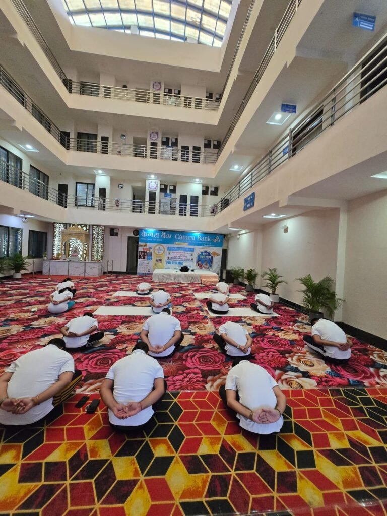 योग दिवस 2025 के अवसर पर बंद हॉल में सामूहिक योग करते वयस्क प्रतिभागी