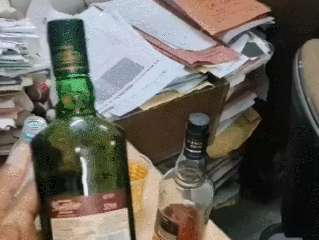 विश्वविद्यालय के कार्यालय में रखी शराब की दो बोतलें, पास में फैली हुई छात्रों की फाइलें और दस्तावेज।